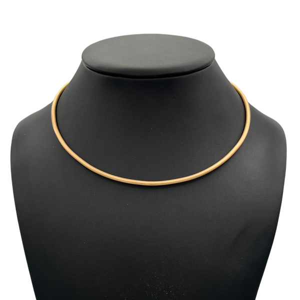 Gold necklace on a black mannequin bust against a white background